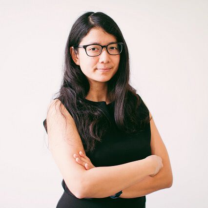 Une jeune femme se tient de trois-quart : elle a les cheveux noirs et longs, des lunettes et sourit légèrement. C’est le portrait de Tiphaine