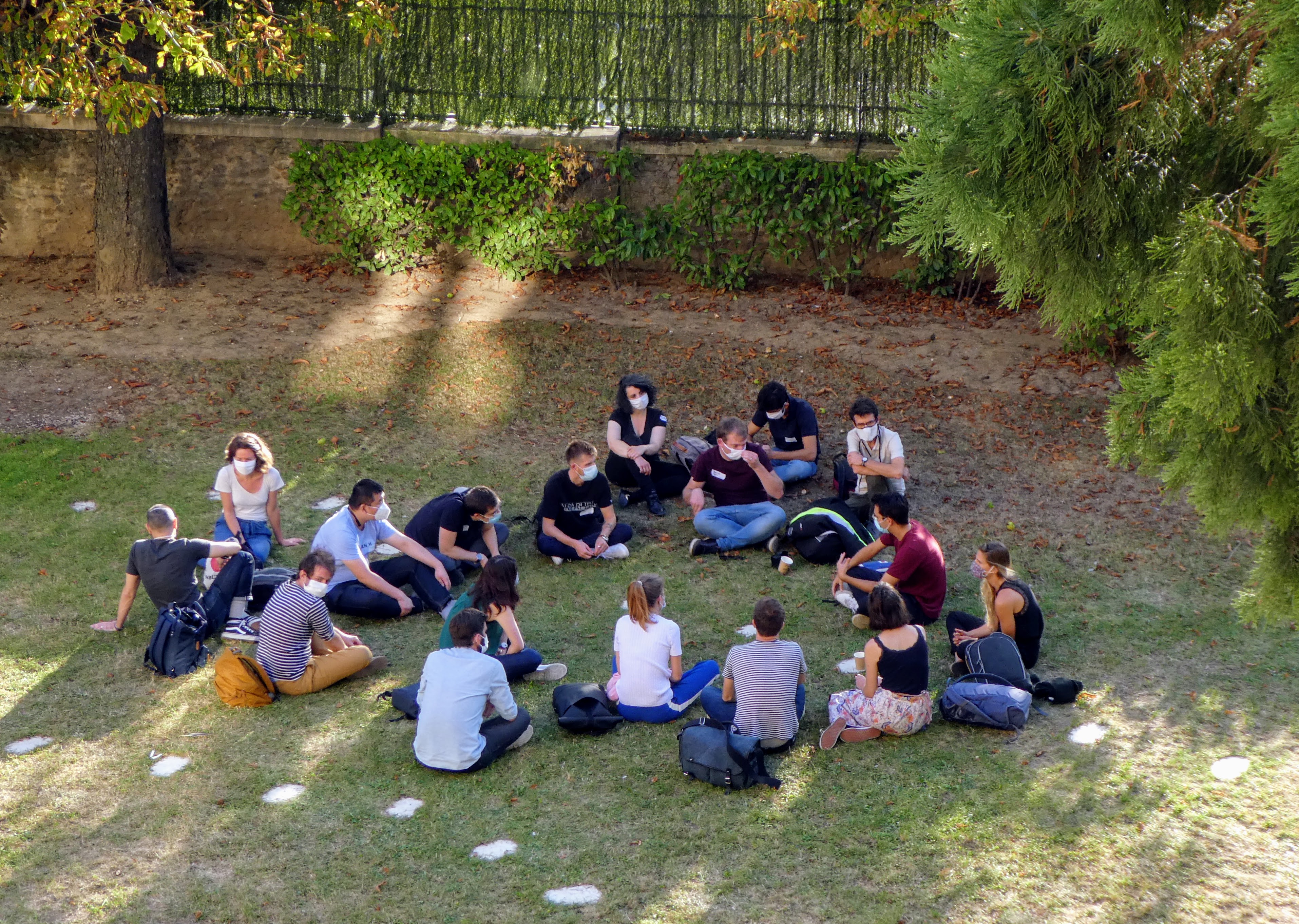 Une vingtaine de personnes sont assises dans l’herbe, en cercle. Elles échangent