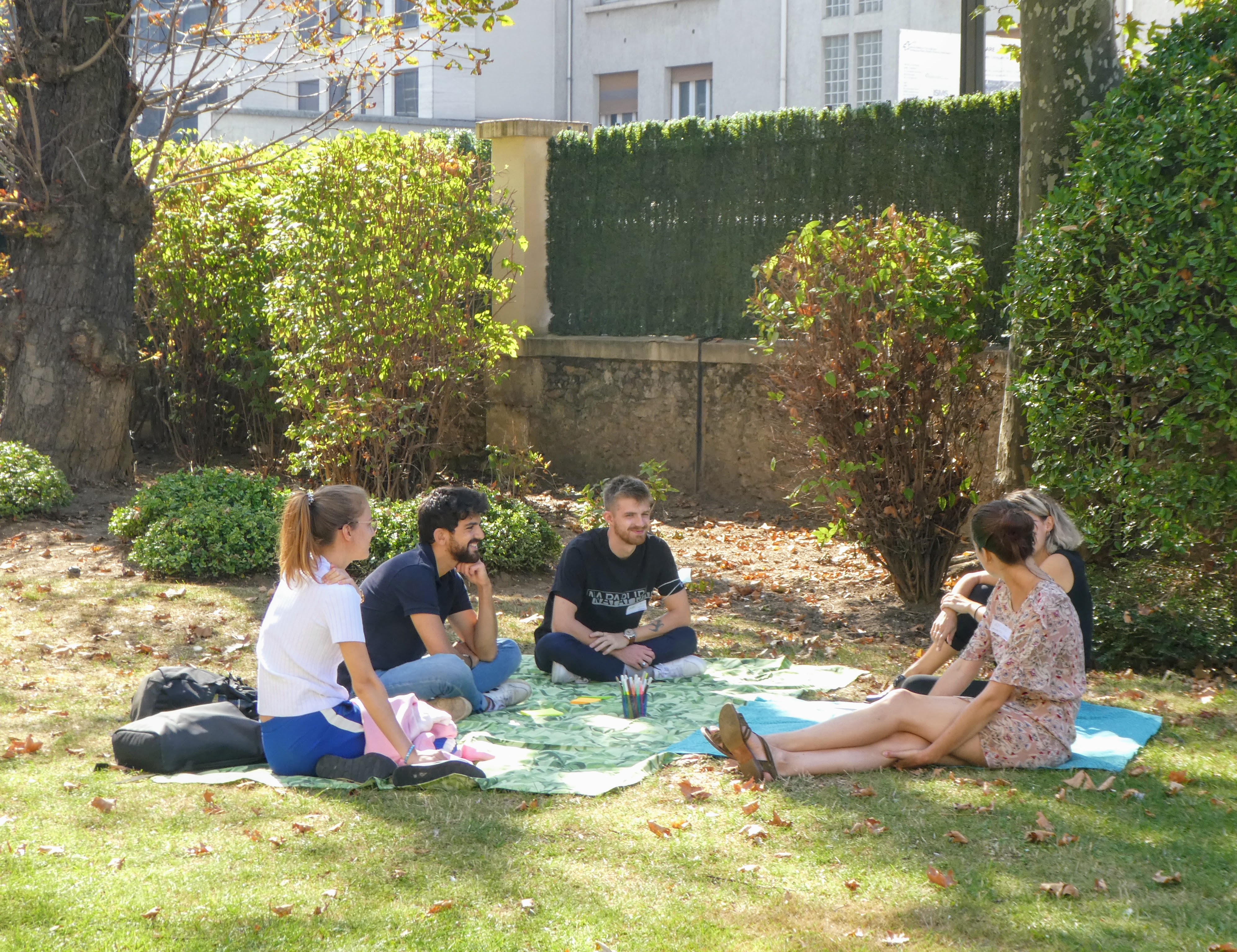 Cinq personnes discutent, assises dans l’herbe. Elles sont souriantes.