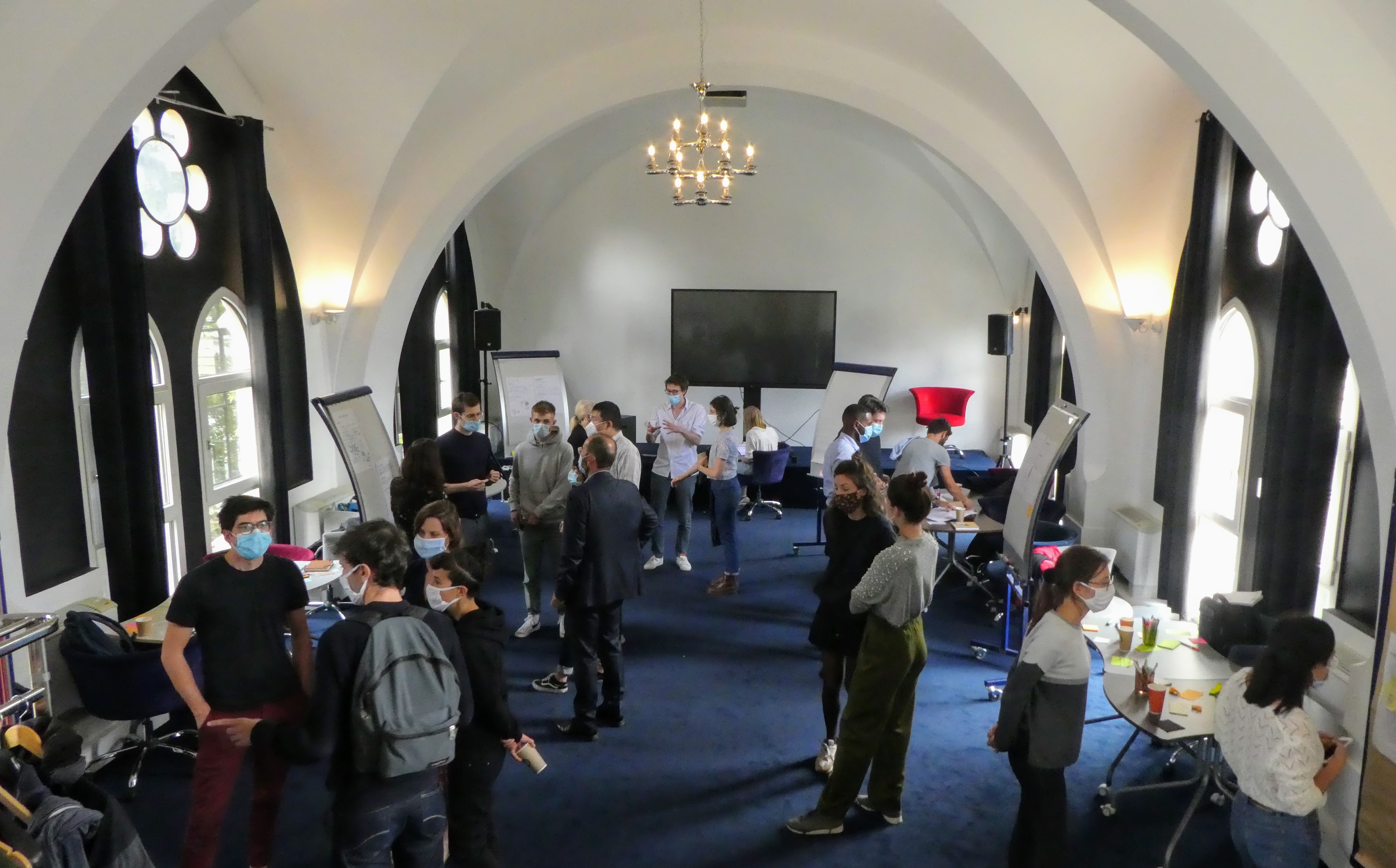 Une vingtaine de personnes sont réunies dans une salle où sont exposés des posters. Les personnes consultent les posters et échangent